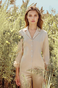 Blonde model in champagne MANITO Diva Feather Trimmed Pajama Set surrounded by wild plants in a golden field.