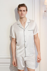 The man is elegant and comfortable in an authentic white short silk pajama set with contrasting trim.