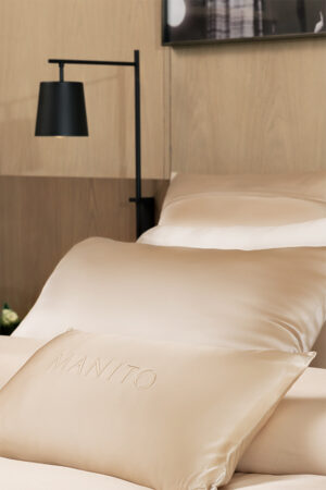 Close-up of MANITO Infinity Silk Duvet Pillowcase Cover with embroidered branding.