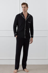 A man stands wearing the full black MANITO Jersey Men's Modal Silk Pajama Set with white piping.