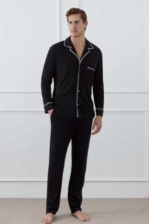 A man stands wearing the full black MANITO Jersey Men's Modal Silk Pajama Set with white piping.
