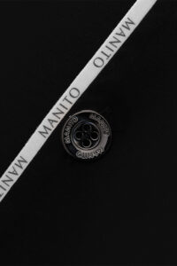 Extreme close-up shot of the MANITO logo button and iconic ribbon on the Jersey Modal Silk Pajama.