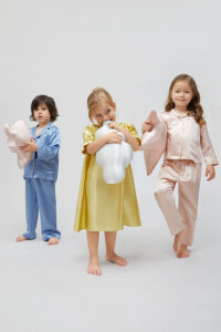 Three children in silk pajamas holding silk cushions shaped like a star, cloud, and elephant.