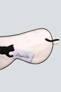 Close-up of MANITO cat eye mask in light pink with black cat embroidery and purple logo patch.