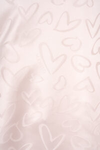 Details of MANITO Loving Silk Nightdress with tonal heart motifs and faint logo, showcasing texture and softness.