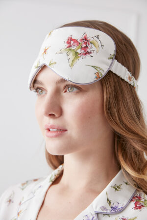Woman wears a Lrisette silk eye mask adorned with a vivid floral design, showcasing soft pastel colors and intricate flower illustrations, adding a delicate and elegant touch.