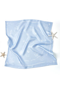 Wrinkled flat lay of MANITO Ocean Blue Silk Scarf with soft marine prints and starfish accessories on the corners.