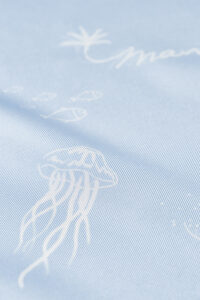 Macro view of jellyfish print and palm illustration on the smooth surface of the MANITO Ocean Blue Silk Scarf.