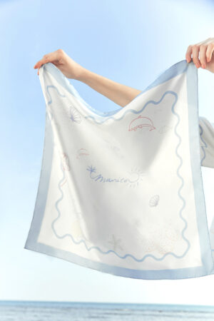 Hands holding up MANITO Ocean Wave Silk Scarf in sunlight, showing marine animal prints and soft pastel colors.