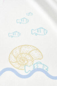 Macro shot of MANITO Ocean Wave Silk Scarf showing yellow seashell and swimming fish on fine mulberry silk texture.