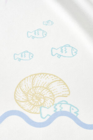 Macro shot of MANITO Ocean Wave Silk Scarf showing yellow seashell and swimming fish on fine mulberry silk texture.