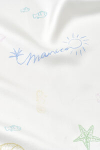 Detailed view of MANITO Ocean Wave Silk Scarf with brand signature, sun symbol, and marine elements.