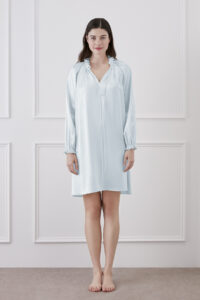 A woman standing and smiling in baby blue silk dress with ruffle trim and lantern sleeves.