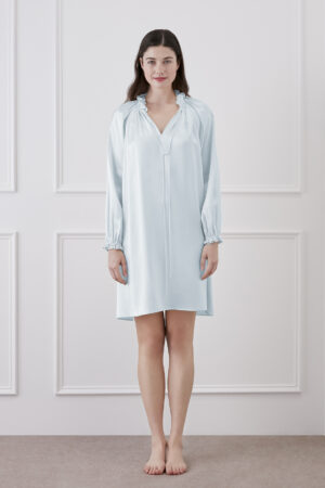 A woman standing and smiling in baby blue silk dress with ruffle trim and lantern sleeves.