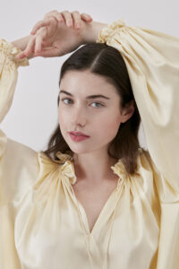 Elegant woman in bellflower yellow silk dress, close up detail of dress with ruffle trim and lantern sleeves.