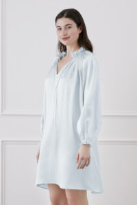 Stylish woman in baby blue silk dress with ruffle trim and lantern sleeves, Standing and Smiling.