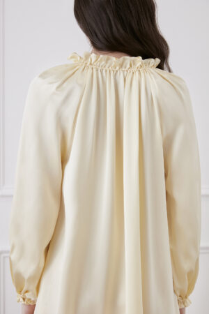 Back view of bellflower yellow silk dress worn by a woman, showcasing ruffle trim collar and sleeves.