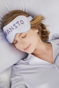 Woman sleeping peacefully wearing a MANITO macaron silk eye mask from the gift box, showcasing relaxation and comfort.