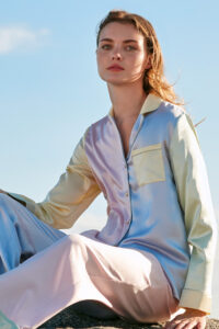 Woman wearing MANITO Macaron Silk Pajama Set seated outdoors, in pastel silk with contrast trim.