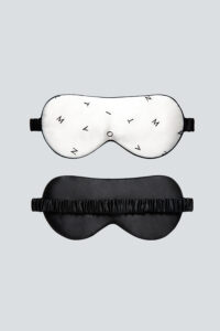 Signature Silk Eye Mask is shown front and back, white with minimalist monogram on the front and black on the reverse.