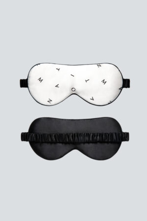 Signature Silk Eye Mask is shown front and back, white with minimalist monogram on the front and black on the reverse.