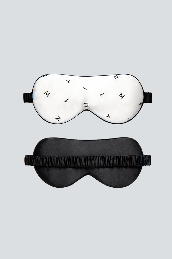 Signature Silk Eye Mask is shown front and back, white with minimalist monogram on the front and black on the reverse.