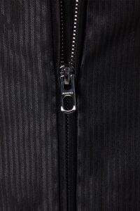 Close-up of Monogram Cotton Silk Hoodie zipper with MANITO logo on glossy textured fabric.