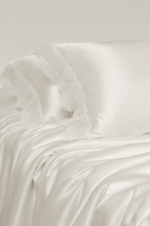 Side view of Moonlight silk bedding, revealing flowing silk folds and soft lace edges.