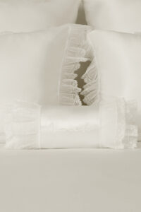 Close-up of Moonlight silk bedding with embroidered bolster and lace-trimmed pillowcases, highlighting ethereal softness.