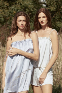 Two women in a natural setting wearing Blooming Camisole & Shorts Set, one in purple and one in white silk.