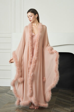 Woman stands in coral New Diva Feather Long Robe, holding the wide hem to show the sweeping feather-trimmed silhouette.