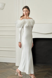 Woman walks in white New Diva Feather Off-the-shoulder Dress, slim silhouette and refined neckline moving gracefully with each step.