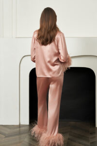 Back view of woman in coral New Diva Feather Pajamas Set, smooth satin drape and fluffy feather hems showing a light, swaying finish.