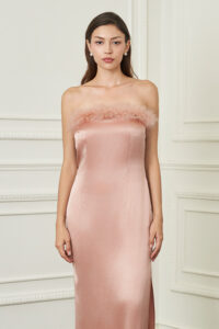 Woman faces forward in coral New Diva feather strapless dress, feather-trimmed neckline and gentle sheen bringing romantic charm.