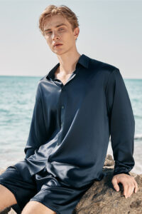 Model sitting on a rock wearing MANITO Ocean Blue Dolphin Men's Pajama Set with long sleeves.