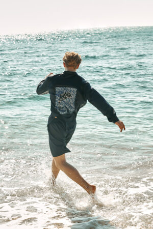 Action shot of model running into ocean in MANITO Ocean Blue Dolphin Men's Pajama Set.