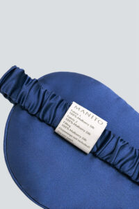 Back side of MANITO Ocean Blue Dolphin Silk Eye Mask showing brand label and ruched silk strap.