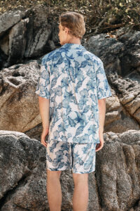 A man stands against a rocky backdrop, showcasing the back view of the MANITO Ocean Blue Men's Silk Short Pajama Set.