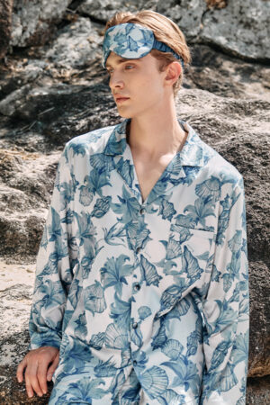 Man wearing MANITO Ocean Blue Men's Silk Eye Mask, sitting on rocks with a serene expression.