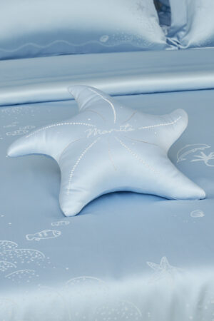 MANITO blue Ocean Starfish Throw Pillow on silk bedspread with embroidered shells and sea creatures.