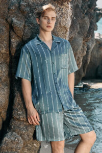 Man wearing MANITO Ocean Stripe Men's Short Pajama Set by the rocks, showcasing the relaxed beachwear style.