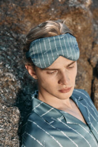 Model with closed eyes wearing MANITO Ocean Stripe Men's Silk Eye Mask in natural light.