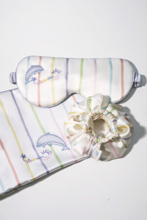 Close-up of MANITO silk eye mask, pillowcase, and scrunchie with a pastel stripe design and delicate embroidery.