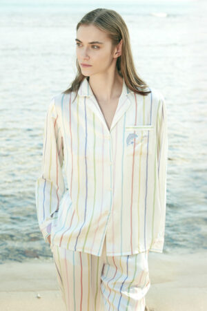 Model wearing MANITO rainbow striped long sleeve shirt and pants by the ocean.