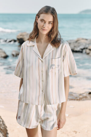 Model wearing MANITO rainbow striped shirt and shorts by the beach, featuring a relaxed fit.