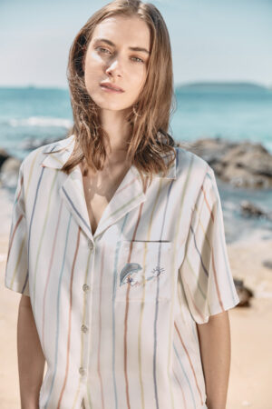 Close-up of MANITO rainbow striped shirt with an embroidered dolphin and sun on the chest pocket.