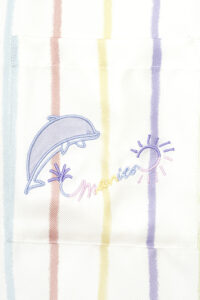 Detailed embroidery of a dolphin and sun on MANITO rainbow striped shirt pocket.