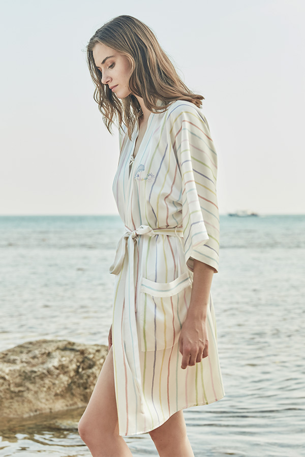 A woman wearing MANITO Ocean Stripe Silk Short Robe by the ocean.