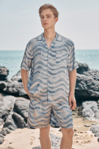 Model wearing MANITO Ocean Wave Men's Short Pajama Set on beach rocks.