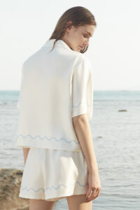 Back view of MANITO Ocean Wave Silk Women's Short Pajama Set showcasing wave hem detailing against a coastal backdrop.